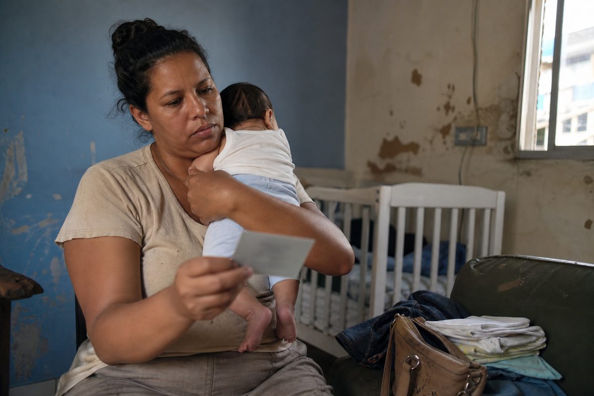 Mãe brasileira com bebê observa uma carteira de trabalho desfocada ao lado do berço.