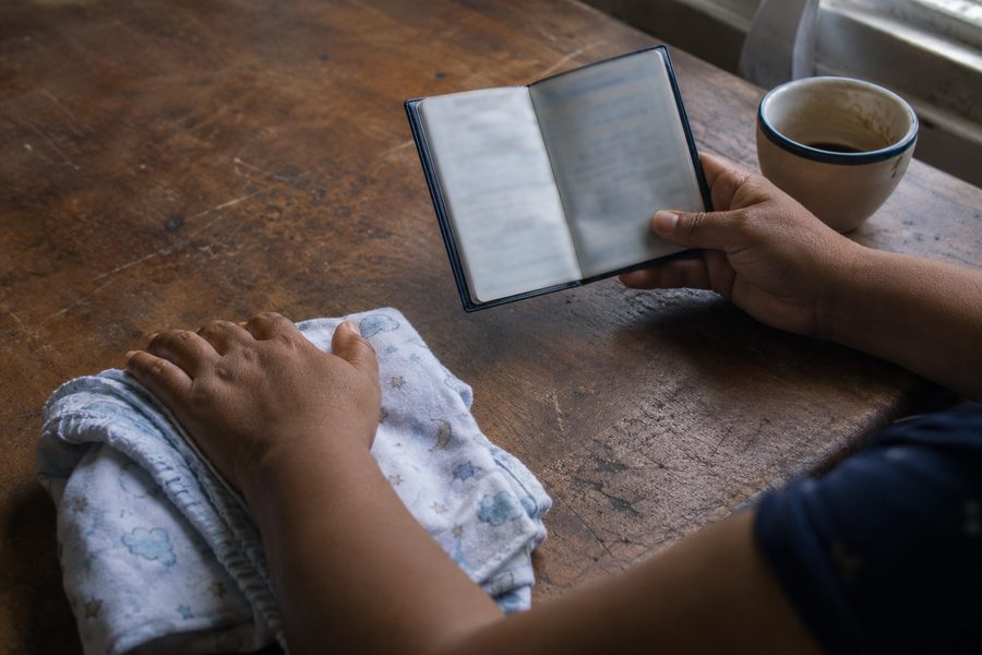 Mãos de mãe sobre a mesa, ao lado de uma manta de bebê e uma carteira de trabalho