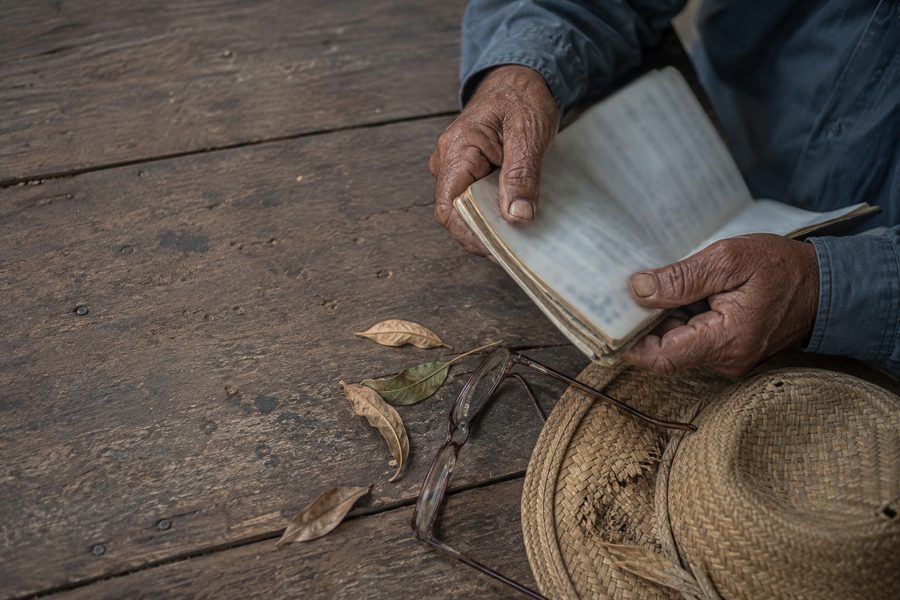 Mãos calejadas de trabalhador rural sobre uma mesa de madeira, com caderneta e chapéu
